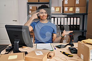 Hispanic man with curly hair working at small business ecommerce confused and annoyed with open palm showing copy space and