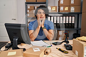 Hispanic man with curly hair working at small business ecommerce tired hands covering face, depression and sadness, upset and