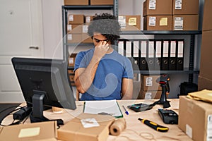 Hispanic man with curly hair working at small business ecommerce tired rubbing nose and eyes feeling fatigue and headache