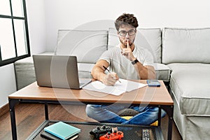 Hispanic man doing papers at home asking to be quiet with finger on lips