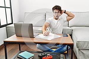 Hispanic man doing papers at home crazy and scared with hands on head, afraid and surprised of shock with open mouth