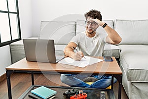 Hispanic man doing papers at home very happy and smiling looking far away with hand over head