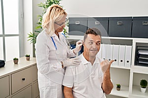 Hispanic man getting medical hearing aid at the doctor pointing thumb up to the side smiling happy with open mouth