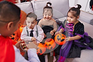Hispanic man and group of kids having halloween party distributing sweets at home