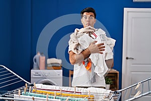 Hispanic man hanging clothes at clothesline making fish face with mouth and squinting eyes, crazy and comical