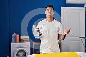 Hispanic man holding electric iron puffing cheeks with funny face