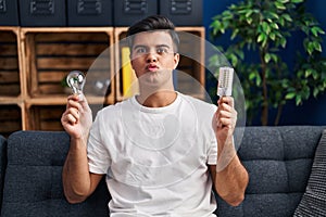 Hispanic man holding led lightbulb and incandescent bulb looking at the camera blowing a kiss being lovely and sexy