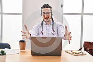 Hispanic man with long hair working using computer laptop looking at the camera smiling with open arms for hug