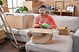 Hispanic man moving to a new home unpacking clueless and confused expression