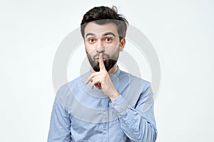Hispanic man placing finger on lips as if to say, shhhhh, be quiet, silence.