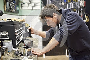 Hispanic man pouring thinner into a cup of black paint on a workshop countertop