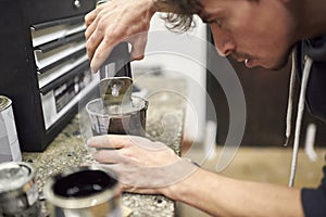 Hispanic man pouring thinner into a cup of black paint on a workshop countertop