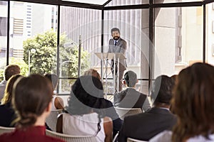 Hispanic man presenting business seminar leaning on lectern