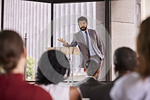 Hispanic man presenting business seminar leaning on lectern