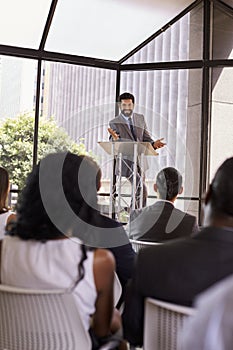 Hispanic man presents business seminar to audience, vertical