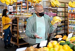 Hispanic man in protective mask looking for bananas in supermarket