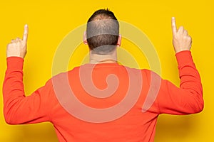 Hispanic man in red sweatshirt pointing up with his index fingers with his back to the camera, isolated on yellow