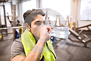 Hispanic man resting in gym, drinking water, towel around neck