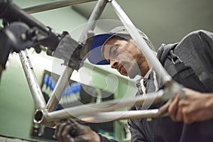Hispanic man sanding a bicycle frame at his workshop