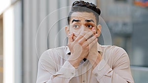 Hispanic man scared businessman boss stands in city covering mouth with hands from shock fear blab out secret frightened