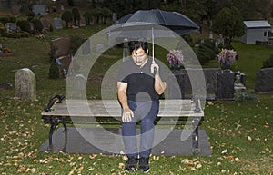 Hispanic man sitting on bench with lowered head in cemetery