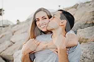 A Hispanic man is sitting with his girlfriend on the stones of a breakwater