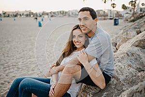 A Hispanic man is sitting with his girlfriend on the stones of a breakwater