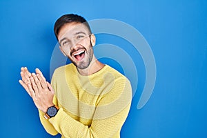 Hispanic man standing over blue background clapping and applauding happy and joyful, smiling proud hands together