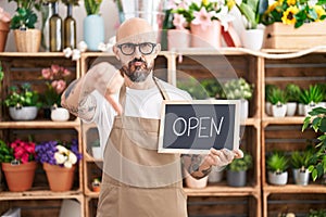 Hispanic man with tattoos working at florist holding open sign with angry face, negative sign showing dislike with thumbs down,