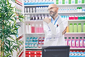 Hispanic man with tattoos working at pharmacy drugstore hugging oneself happy and positive, smiling confident