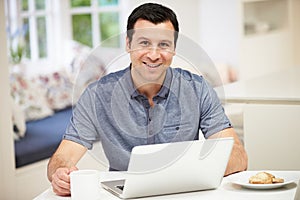 Hispanic Man Using Laptop In Kitchen At Home