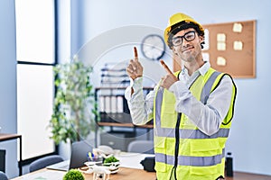 Hispanic man wearing architect hardhat smiling and looking at the camera pointing with two hands and fingers to the side