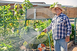 Hispanic Man Wearing Hat Watering Crop in a Community Garden