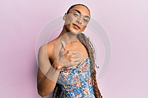 Hispanic man wearing make up and long hair wearing elegant corset doing happy thumbs up gesture with hand