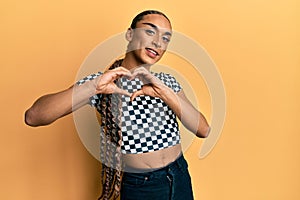 Hispanic man wearing make up and long hair wearing modern clothes smiling in love doing heart symbol shape with hands