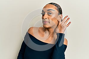 Hispanic man wearing make up and long hair wearing woman fashion clothes smiling with hand over ear listening and hearing to rumor