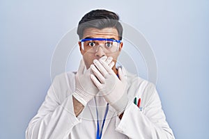 Hispanic man working as scientist shocked covering mouth with hands for mistake