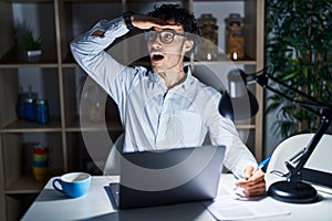 Hispanic man working at the office at night very happy and smiling looking far away with hand over head