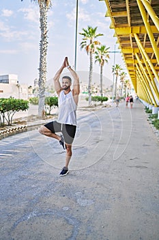 Hispanic man working out doing yoga tree pose outdoors on a sunny day