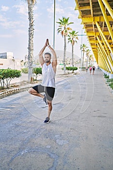 Hispanic man working out doing yoga tree pose outdoors on a sunny day