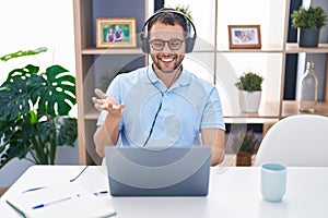 Hispanic man working using computer laptop wearing headphones celebrating achievement with happy smile and winner expression with