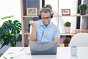 Hispanic man working using computer laptop wearing headphones screaming proud, celebrating victory and success very excited with