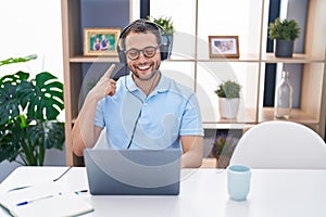 Hispanic man working using computer laptop wearing headphones smiling happy pointing with hand and finger