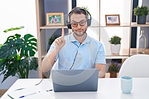 Hispanic man working using computer laptop wearing headphones smiling with an idea or question pointing finger with happy face,