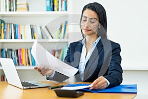 Hispanic mature businesswoman working with documents at desk