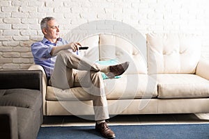 Hispanic mature man watching tv at home