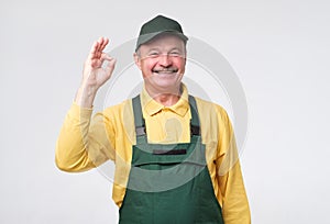 Hispanic mature mechanic in green cap and overalls standing smiling