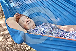 Hispanic mature woman on vacations smiling lying in a blue hammock