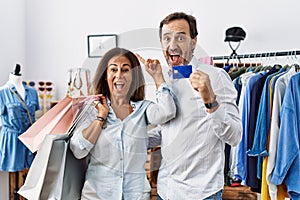 Hispanic middle age couple holding shopping bags and credit card smiling amazed and surprised and pointing up with fingers and