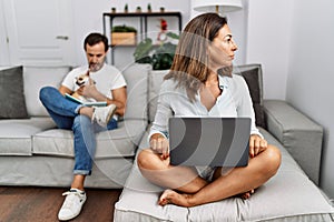 Hispanic middle age couple at home, woman using laptop looking to side, relax profile pose with natural face with confident smile